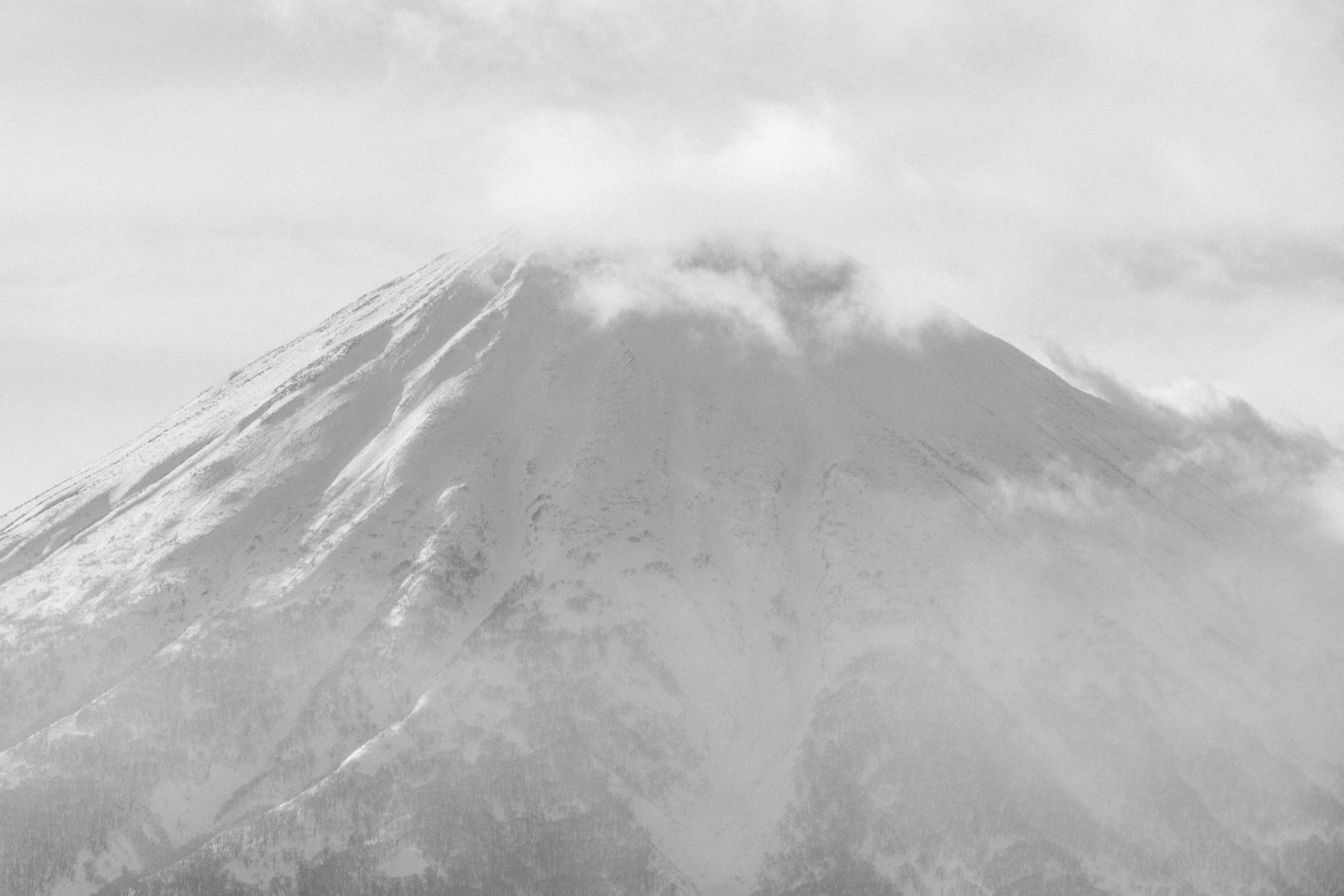 Mount Yotei snow-covered peak shrouded in winter clouds, black and white photograph