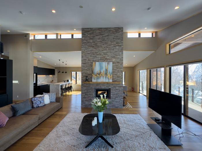Chalet Taiko's modern open-plan living area featuring vaulted ceilings, stone fireplace, and floor-to-ceiling windows