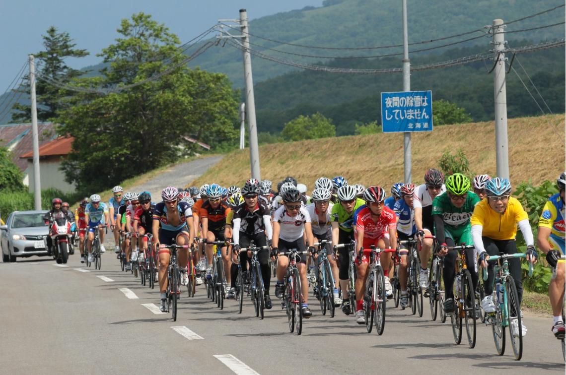 A peloton of cyclist race through Niseko