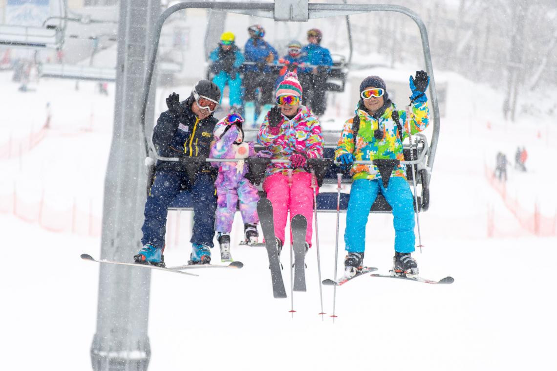 4 Skiers in brightly coloured jackets sitting on a chairlift