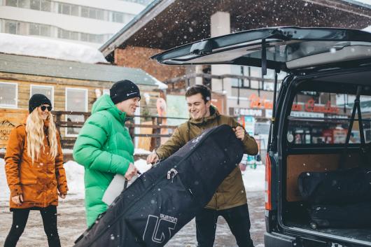 A man helps another to load a bag into a black van at the Hirafu Welcome Center