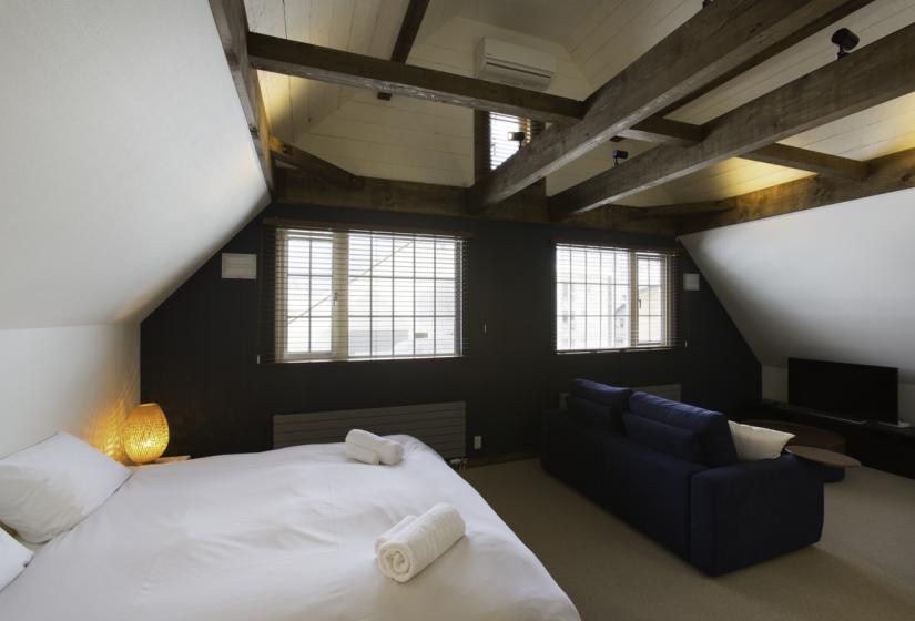 bedroom with small sofa, tv, and high ceilings with wooden support beams