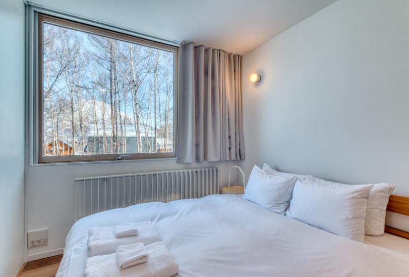 a double bed with folded towels and a window behind