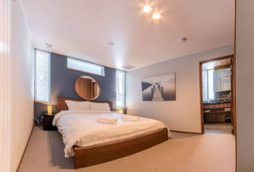 Double bed with white cover below a circle mirror