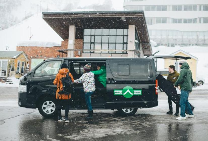 Ski luggage is loaded into a black van on a snowy day