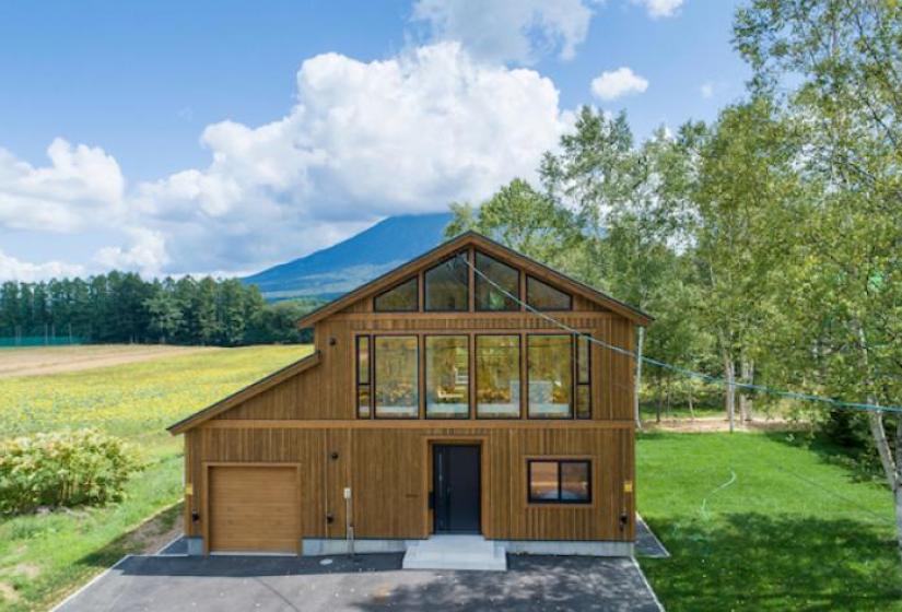 A large wooded house with double pitched roof and blue skies behind