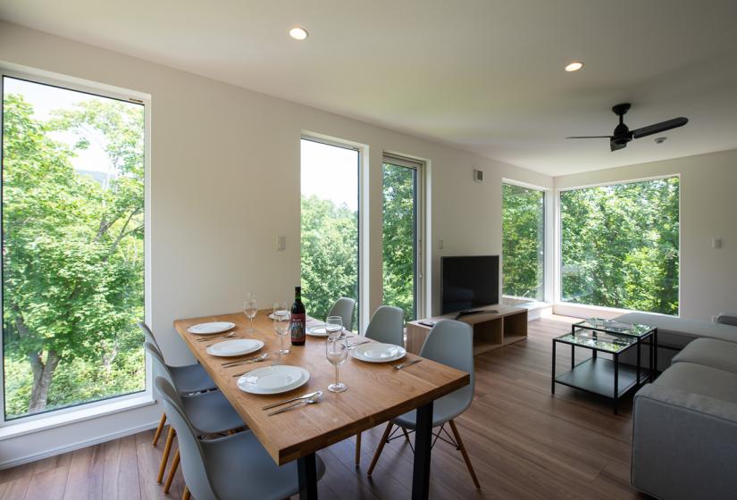 A table set with plates and wine glasses with large windows with a view to leafy surrounds