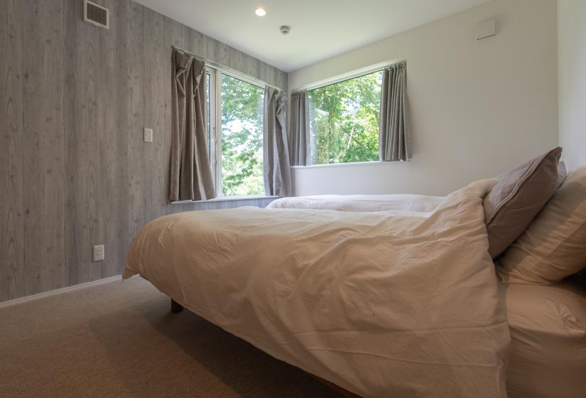 The side of a bed and view of greenery through 2 windows.