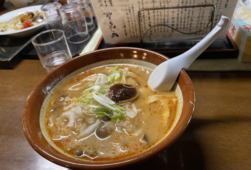 A bowl of ramen noodles with a white spoon.