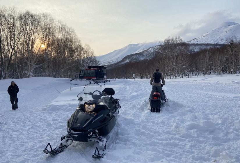 A snowmobile and snow cat at sunset. 