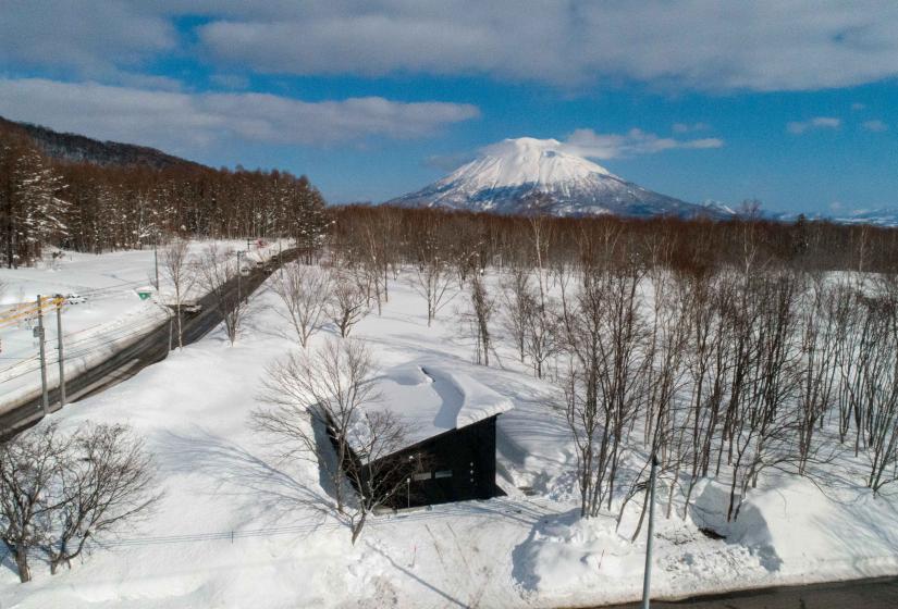 A drone shot of a house in the snow with Mount Yotei behind.