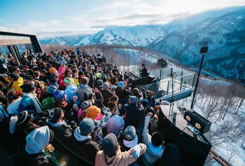 A DJ plays for a crowd amongst snowy hills