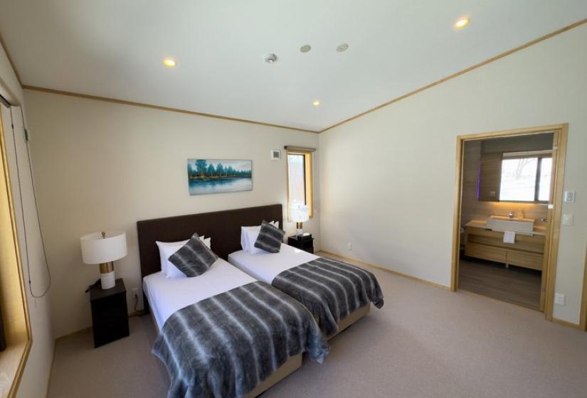 Niseko Chalet Taiko bedroom with split king bed and mountain photography, ensuite bathroom doorway visible