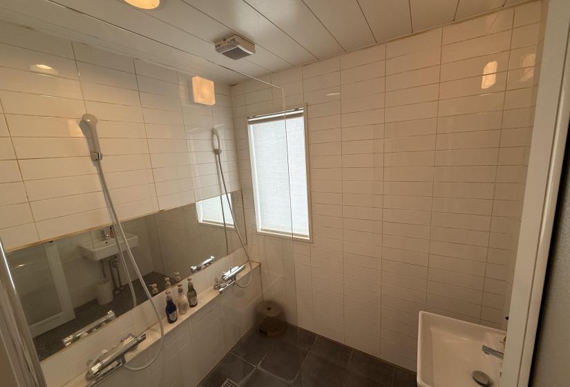 Traditional Japanese bathroom at Yutaka Townhouses featuring deep soaking tub, white tiled walls, and bright natural lighting perfect for relaxing after Niseko ski adventures.