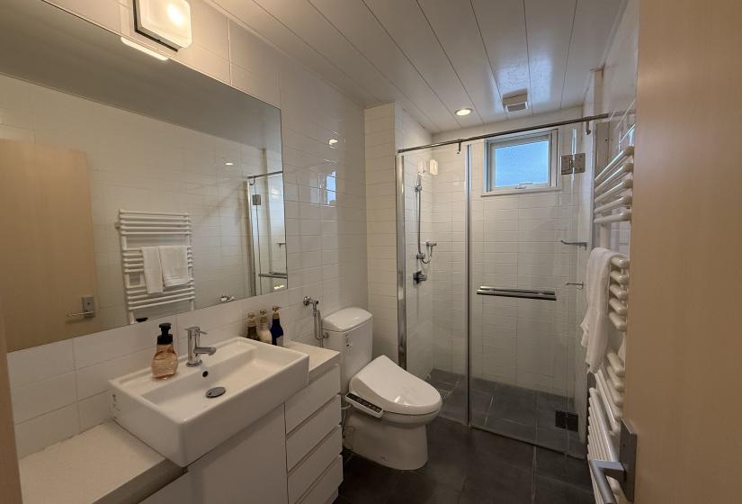 Contemporary bathroom at Yutaka Townhouses with modern vanity, Japanese washlet toilet, heated towel rack, glass shower enclosure, and sleek white tiling, offering premium comfort for guests enjoying Niseko ski holidays.