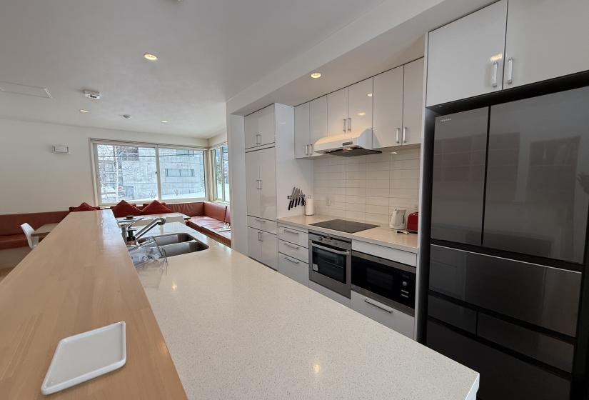 A white kitchen bench and stove and fridge behind