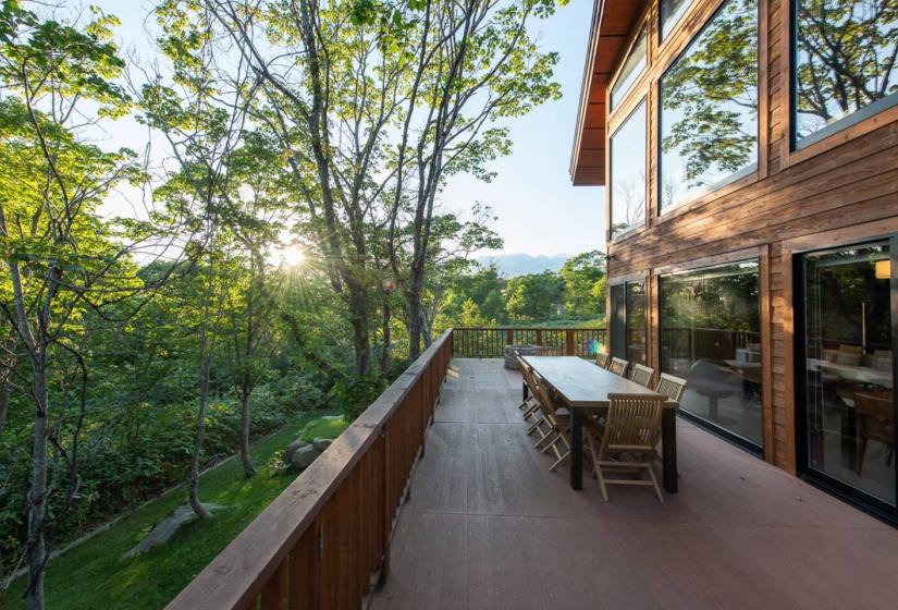 Beautiful outdoor deck at Annupuri Niseko chalet with wooden dining furniture surrounded by lush green forest views