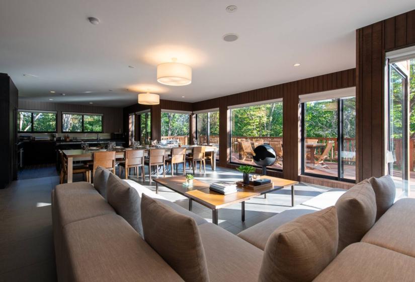 Spacious Annupuri Niseko chalet living area with comfortable sofas, dining table and panoramic forest views through floor-to-ceiling windows