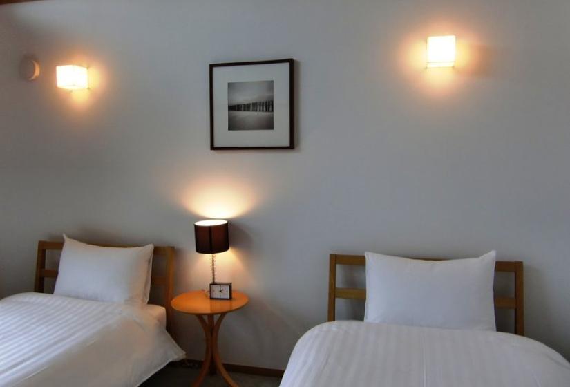 Twin bedroom with two single beds with white linens, wooden headboards, bedside table with lamp, wall sconces, and framed artwork on the wall at Chalet Creekside.