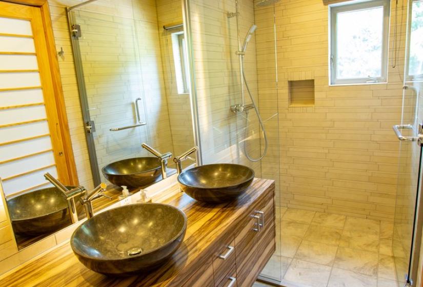 Modern bathroom with wooden ceiling, wooden vanity with vessel sink, large mirror, stone tile floor, and glass shower enclosure at Chalet Creekside.