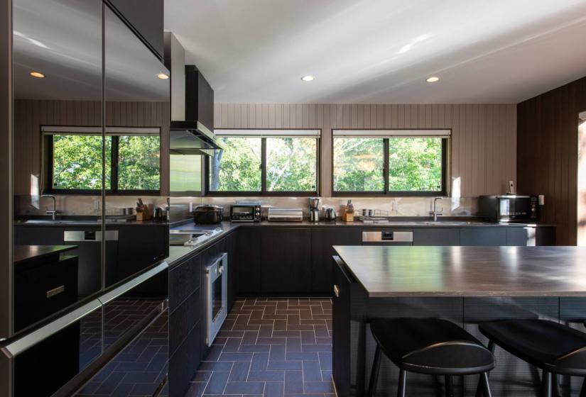 Modern kitchen in Niseko luxury chalet with dark cabinetry, island counter and forest views through large windows