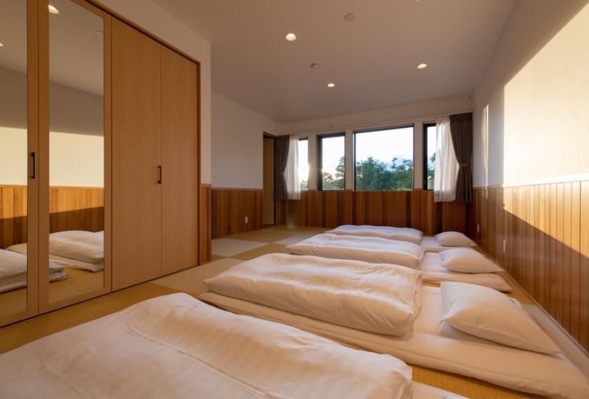Traditional Japanese tatami room in Chalet Kiraku featuring futon bedding on tatami mats, wooden wall panels, sliding doors with mirrors, and large windows with natural light, offering an authentic cultural sleeping experience in this luxury Niseko ski accommodation.