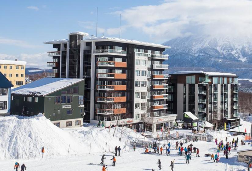 Alpen Ridge Niseko ski-in ski-out luxury accommodation featuring modern multi-story apartment buildings directly on snow-covered slopes with skiers enjoying powder conditions Mount Yotei views and premium winter resort facilities
