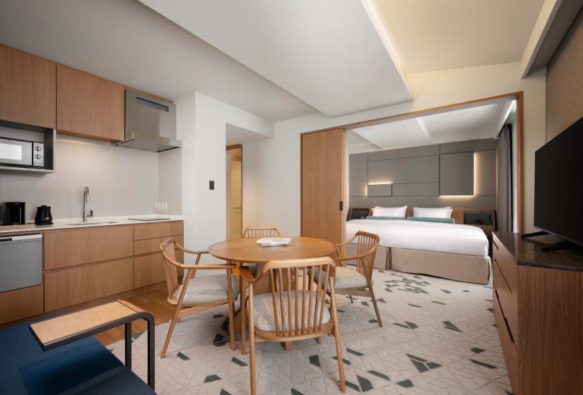 A round dining table beside kitchenette with bed behind